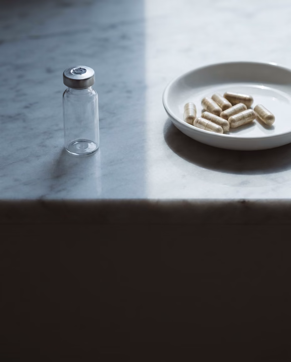 A small unlabeled glass vial on one side of a marble surface and a dish of loose capsules on the other, divided by light and shadow