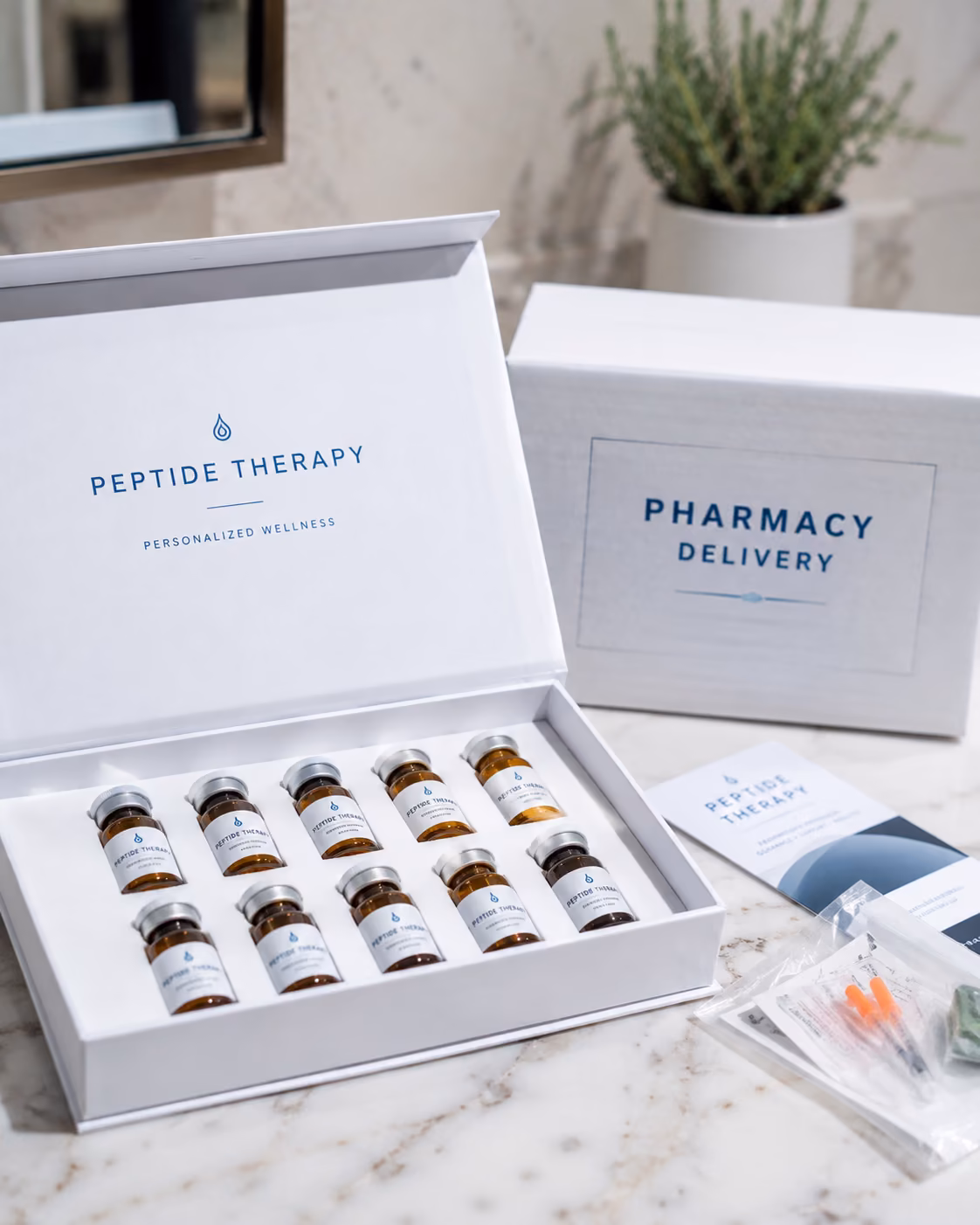A presentation box of capped glass vials on marble beside a second closed box and a sealed syringe
